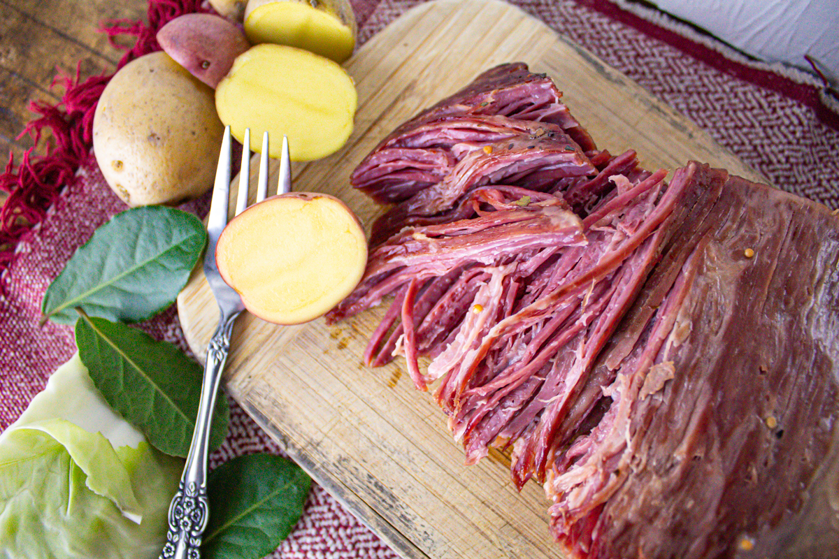 Cooked corned beef on wooden cutting board with potato's.