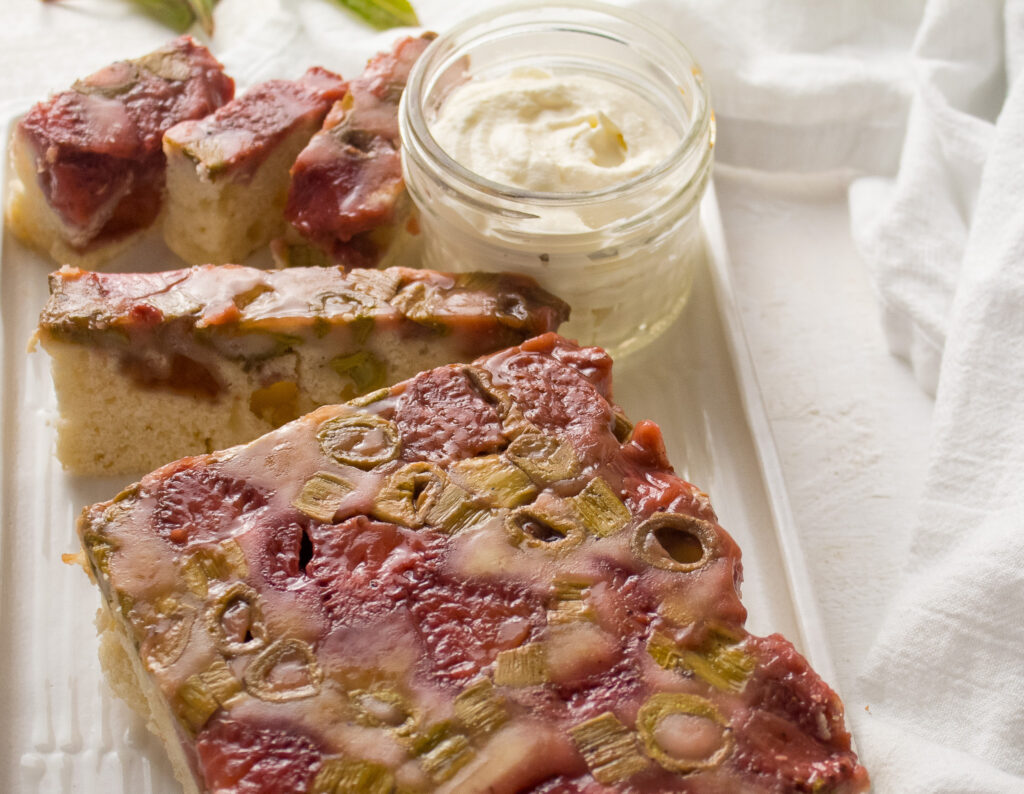 loaf of strawberry and knotweed upside down cake with jar of white whipped cream on plate