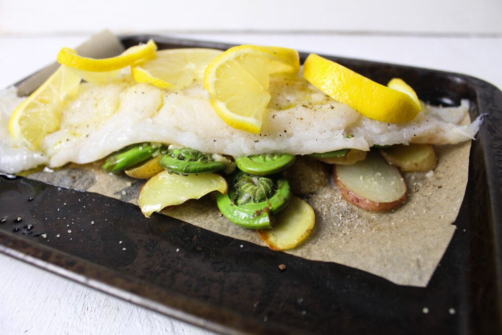 haddock over fiddlehead ferns with lemon slices.