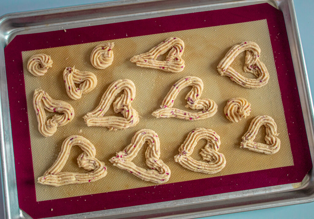 raspberry rose and white chocolate cookies piped into heart shapes on cookie pan.