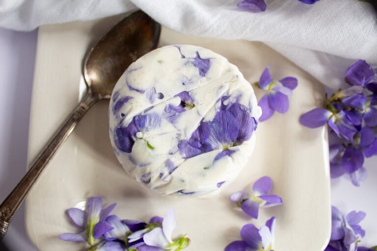Vanilla ice cream with violet flowers mixed in, garnished with scattered violet blossoms, a beautiful and delicious floral dessert.