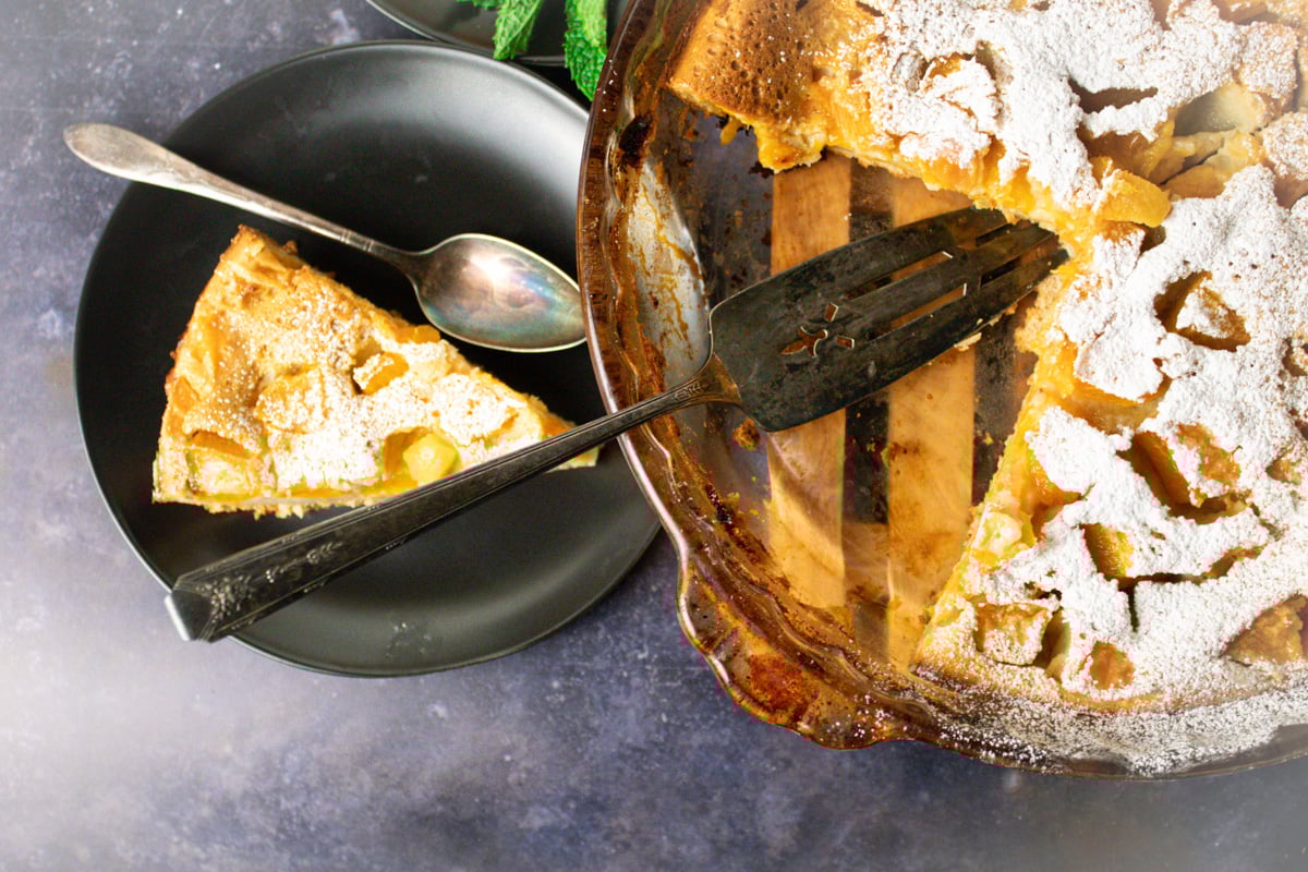 slice of apricot clafoutis on plate next to full pie.
