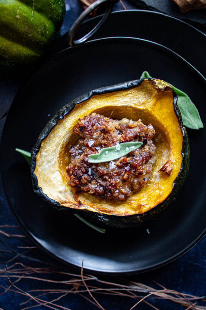 Sausage stuffed acorn squash on black plate with sage leaf in center