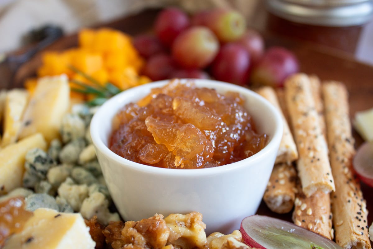 a bowl of apple cider jam on a cheese board surrounded by cheese and crostini.