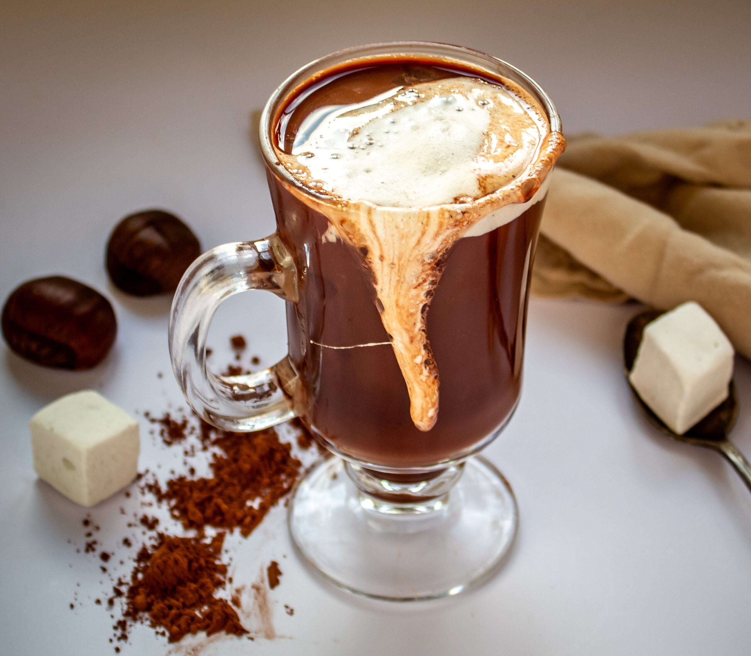 cup of hot chocolate in glass mug with melted marshmallow melter over top.