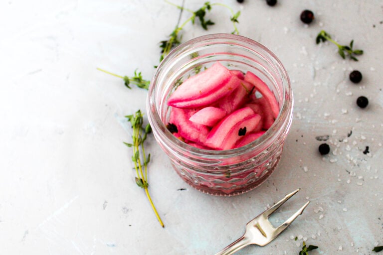 pickled red onion in glass jar with thyme herb and juniper berries.