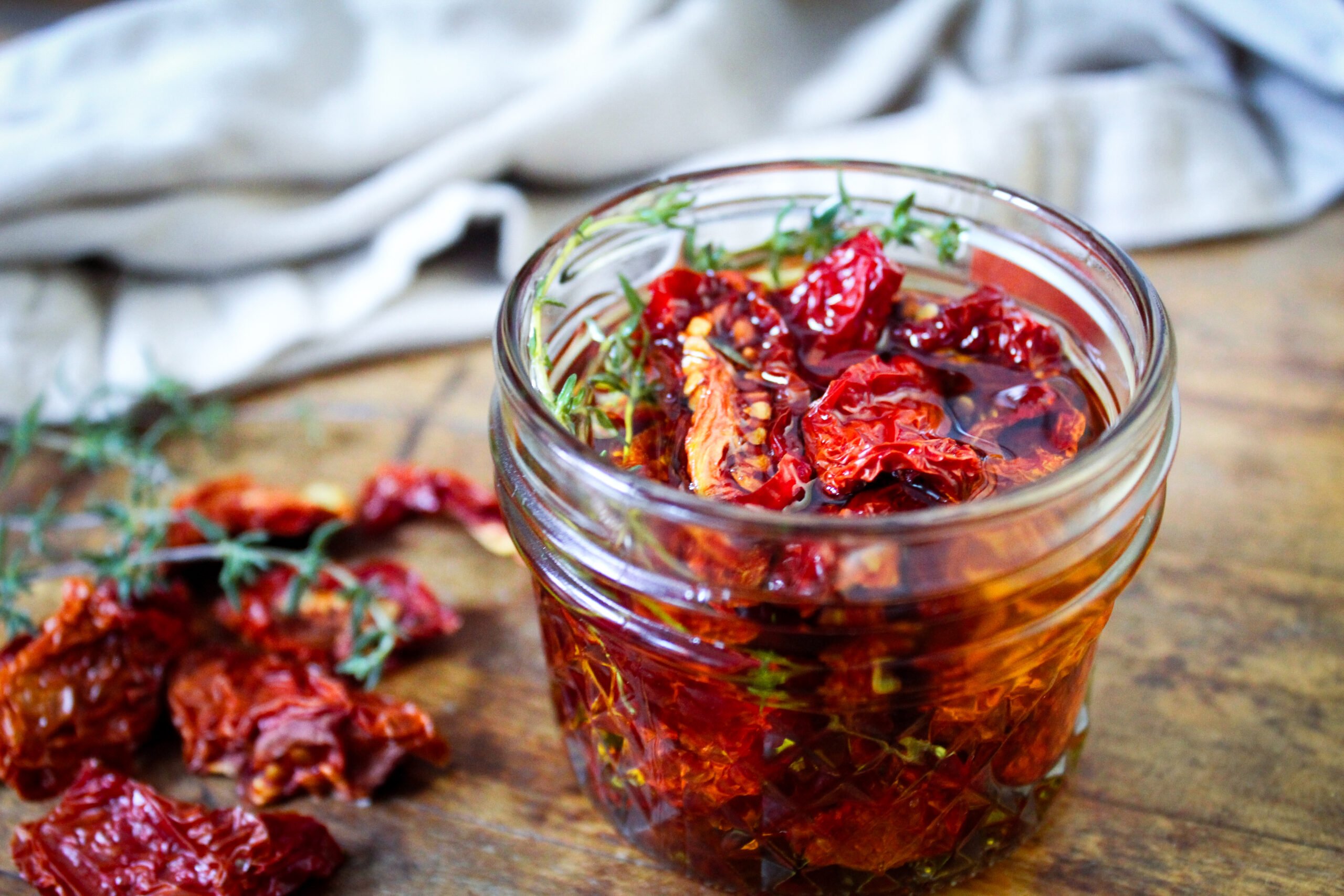 jar of sundried tomatoes with sprigs of thyme in olive oil on wooden table.