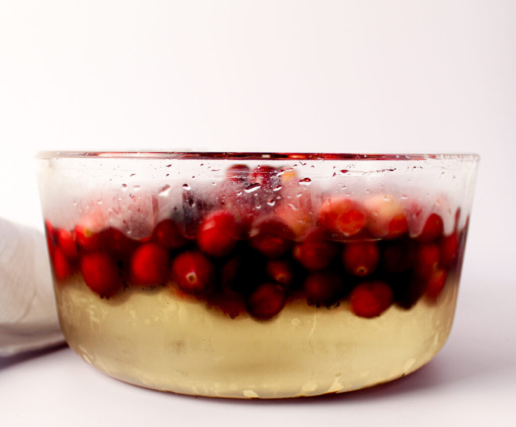 cranberries soaking in clear glass bowl in sugar syrup.