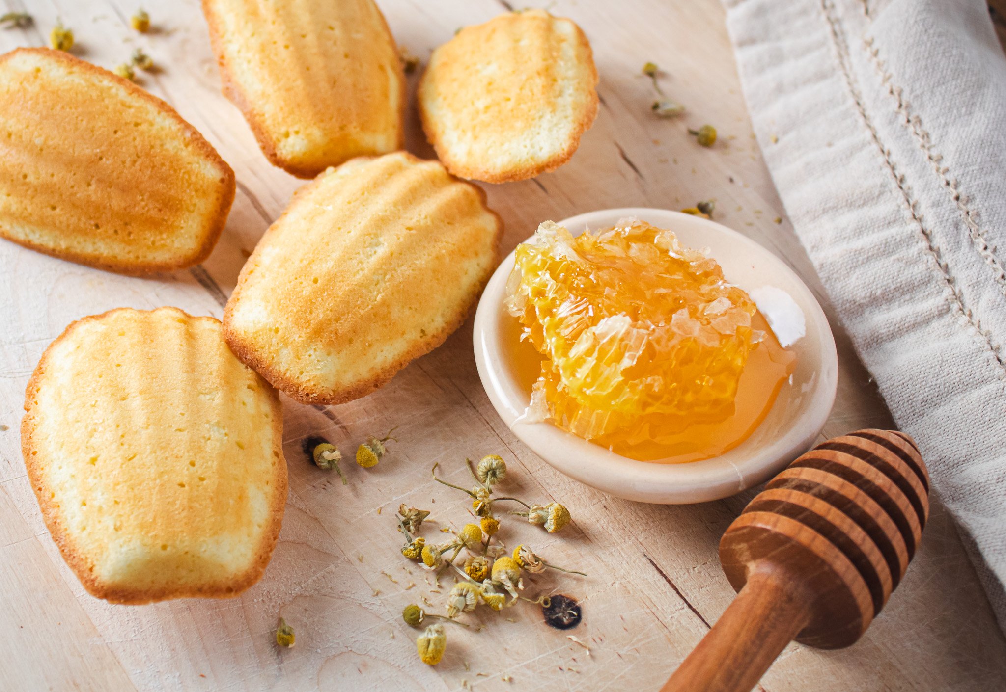 honey bowl next to chamomile honey madeleines with scattered chamomile flowers .