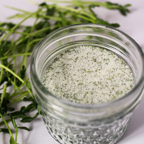 peashoot suagr in glass jar with fresh pea shoots surrounding.