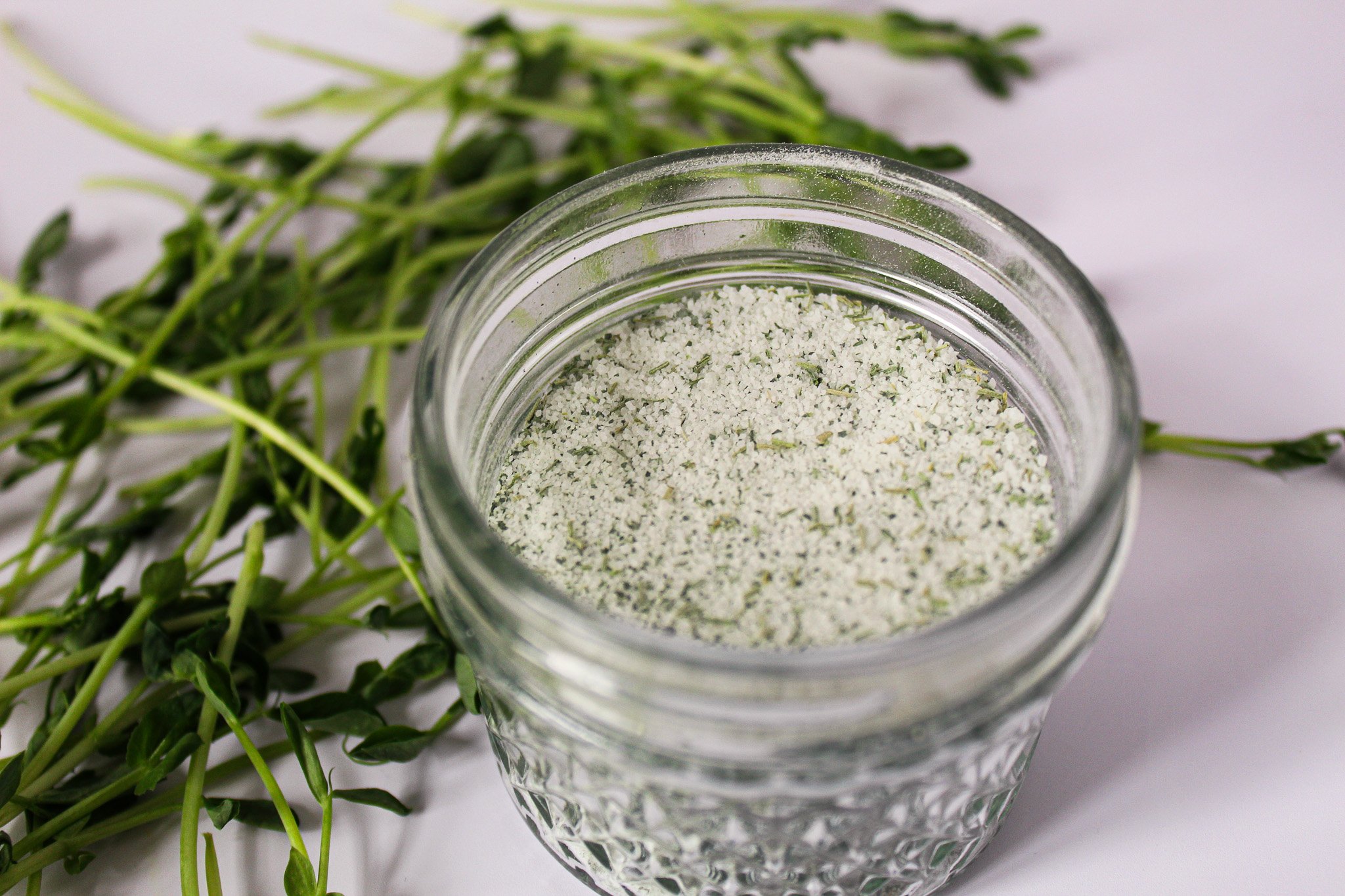 peashoot suagr in glass jar with fresh pea shoots surrounding.